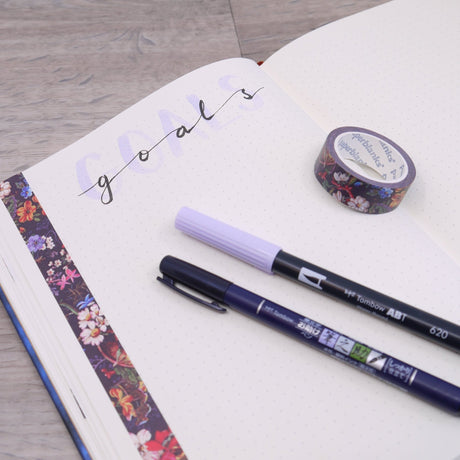 Alla produkter. En anteckningbok med pennor och en rulle washi tape.I boken står det Goals skrivet med de två pennorna. - Tidformera