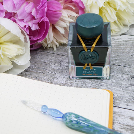 Vacker bläckflaska från Herbin står bredvid en anteckningsbok och en glaspenna. - Tidformera