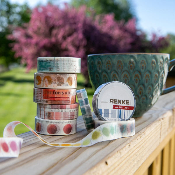 Dekoration. Washi tape rullar staplade på hög. Bilden är tagen utomhus med blommande träd och kaffekopp i bakgrund. - Tidformera