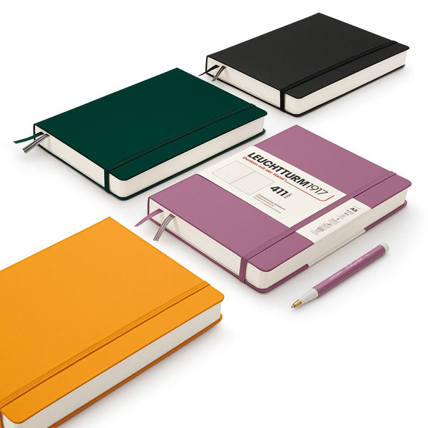 Leuchtturm1917 - 411 - Fyra skrivböcker ligger på ett bord En svart, grön, rosa och gul skrivbok - Tidformera