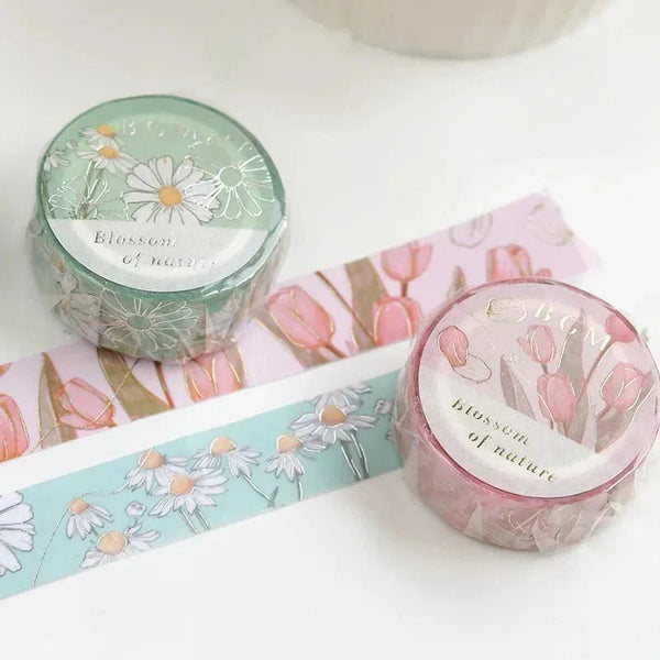 Två förpackningar washi tape i serien Blossom ligger på utrullad washi tape med rosa tulpaner och vita prästkragar. - Tidformera