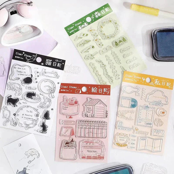 Serier - Clear stamps Diary - Flera förpackningar med clear stamps ligger utspridda på ett bord. Bredvid finns stämpeldynor och lappar som det är stämplat på - Tidformera