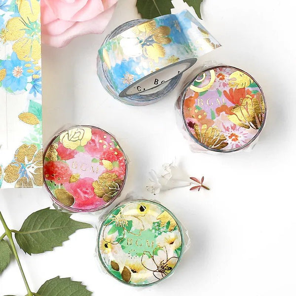 Serien Flower melody. Washi tape från BGM. På ett bord ligger flera rullar med washi tape och motiven är med färggranna blommor. Löv och blommor är utspridda runt rullarna. Tidformera