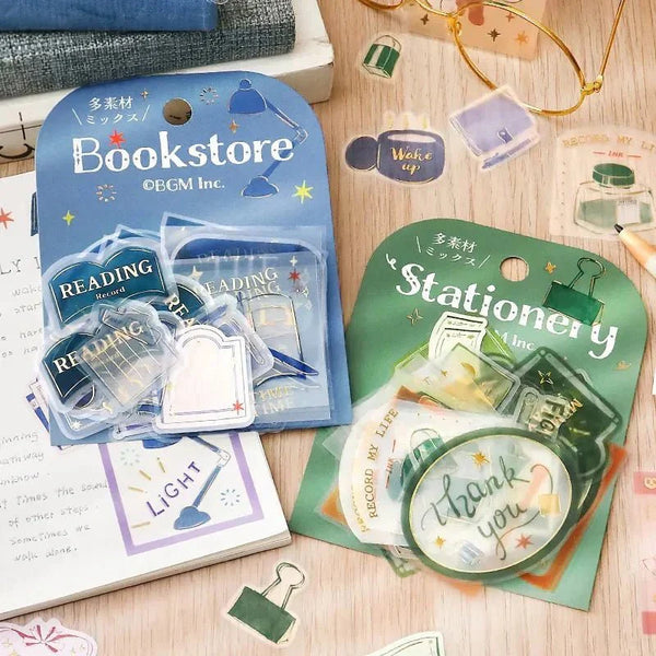 Flake stickers från BGM ur serien Holiday store tour - Två förpackningar med klistermärken ligger på en anteckningsbok. Stickers med clips och bläckflaska ligger utspridd runt. Tidformera