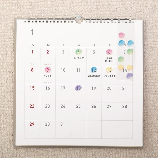 Serier - Kalenderstickers Moln från Midori - En väggkalender hänger på en vägg. På kalendern har det klistrats på små klistermärken i form av moln på vissa av datumen. Tidformera