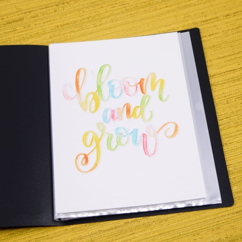 Demopärm A5 Svart från Bantex ligger uppslagen på ett gult bord. I sitter ett ark där bloom and grow är skrivet i lettering.
