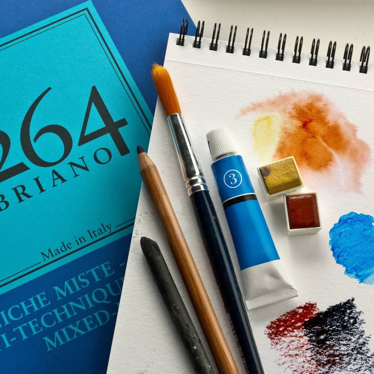 Fabriano 1264 Mixed Media – A5 från  Fabriano. Ett spralblock som det står mixed media på. På ligger ett uppslaget block som det målats i. På den ligger pensel, färger, kol och penna. - Tidformera