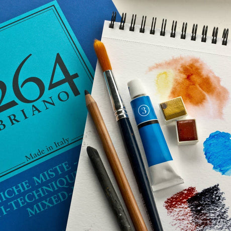 Fabriano 1264 Mixed Media – A5 från  Fabriano. Ett spralblock som det står mixed media på. På ligger ett uppslaget block som det målats i. På den ligger pensel, färger, kol och penna. - Tidformera