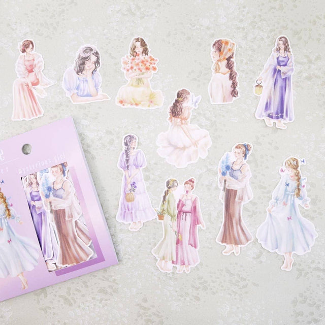 Flake stickers Amie - Mysterious girl från Mind Wave. En förpackning och stickers ligger utspridda. Motiv med kvinnor i fina klänningar - Tidformera