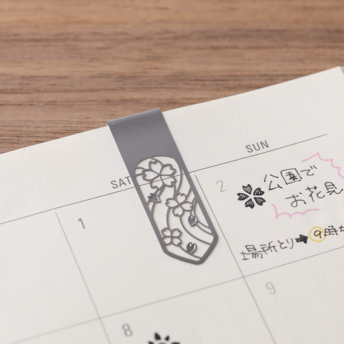 Ett silverfärgat bokmärke med motiv med blommor sitter fast på en sida i en kalender. - Clip Bookmarker Flower från Midori