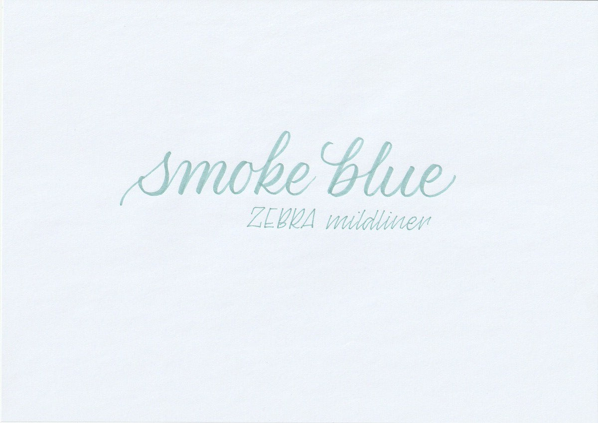 Handskriven text med orden "smoke blue" och "ZEBRA mildliner" i blå färg, skriven med Zebra Mildliner Brush Pen i färgen Smoke Blue.