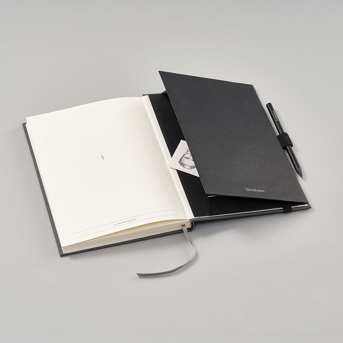 Patch Pocket - Black från Semikolon. Svart självhäftande ficka med elastiskt pennållare. Fickan sitter i en anteckningsbok. - Tidformera