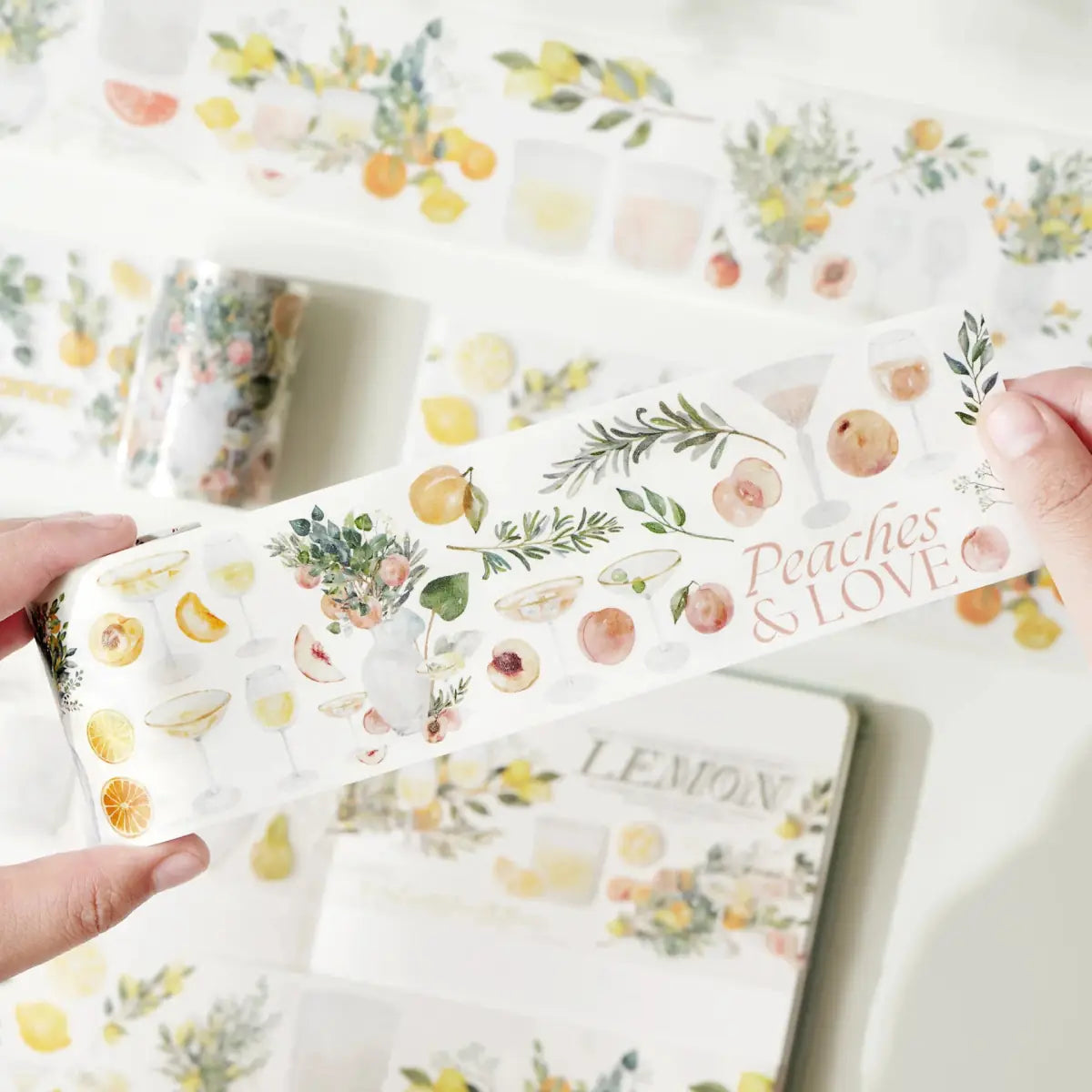 Sticker Washi Tape - Pre - cut - Mediterranean Breeze - 60 mm från Washi Tape Shop. Händer som visar klistermärken på rulle. Motiven är citrusfrukter och persikor, drinkar och kvistar.  -Tidformera
