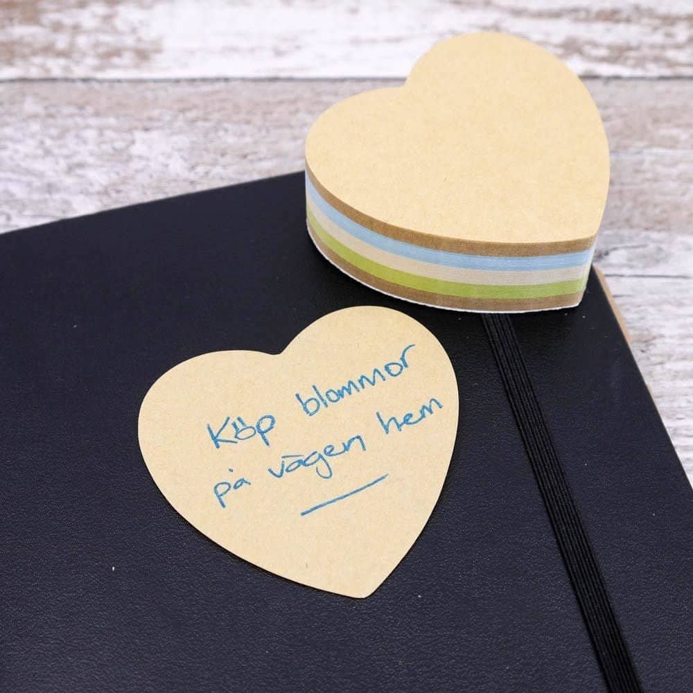 Ett hjärtformat post-it block ligger på en anteckningsbok. Ett papper från blocket är utdraget och skrivet på.