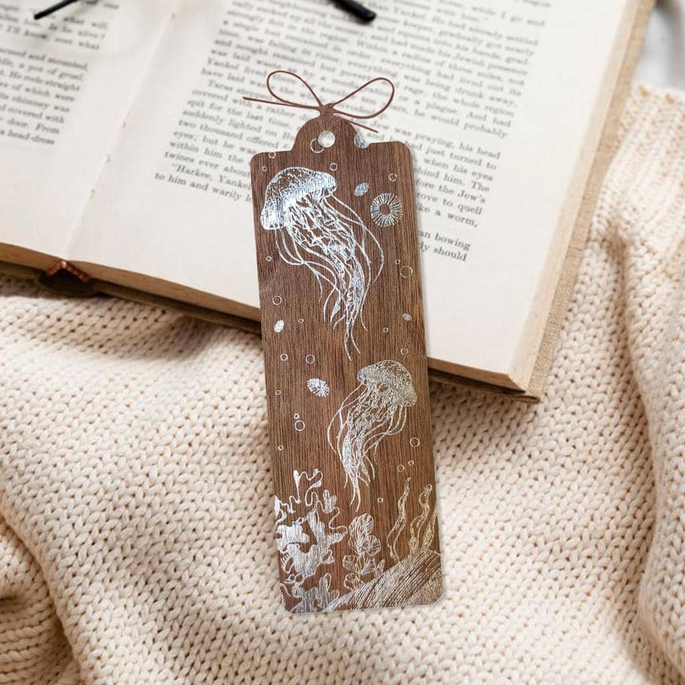 Bokmärke i trä med maneter ligger på uppslagen bok. Wooden bookmark - Dance of the jellyfish från Cozywood - Tidformera