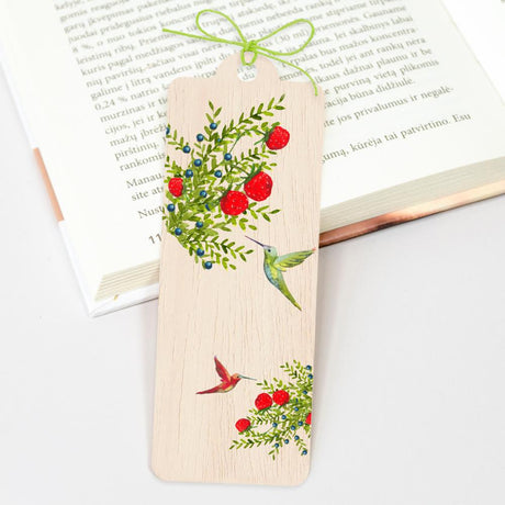 På en bok ligger bokmärket i trä. Motiv på bokmärket är kolibrier och buskar med bär. Wooden bookmark - Hummingbirds från Cozywood - Tidformera