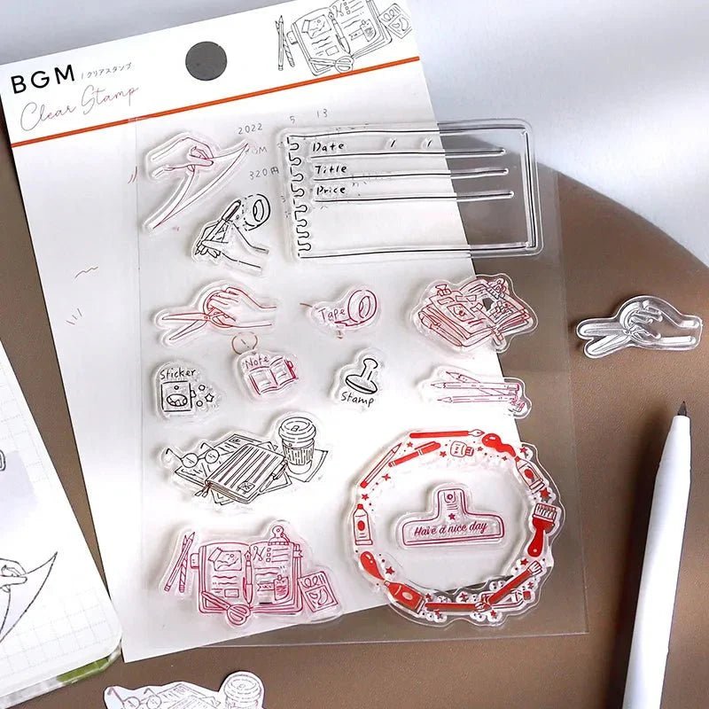 Clear stamps - BGM - En förpackning med clear stamps är öppnad. Motiven på är med skrivande händer, clips och böcker. Bredvid skymtar en anteckningsbok fram samt en penna.  Tidformera