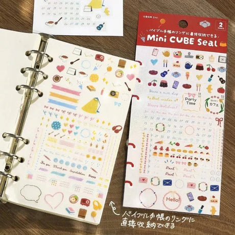 Planner Stickers Sheet 2-pack från BGM - En förpackning med klistermärken ligger bredvid en ringpärm där stickers klistrats in på ett ark - Tidformera