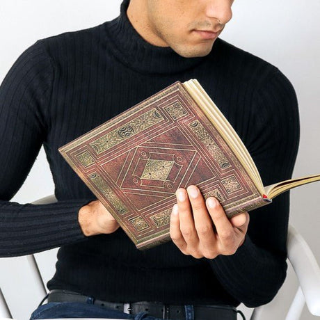 En man som håller i en brun uppslagen anteckningsbok ur serien First Folio från Paperblanks- Tidformera