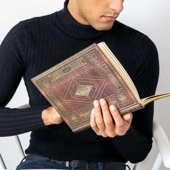 En man som håller i en brun uppslagen anteckningsbok ur serien First Folio från Paperblanks- Tidformera