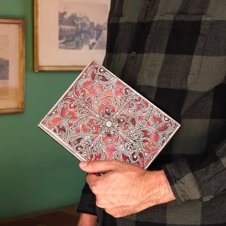 En man som håller i en skrivbok i serien Garnet från Paperblanks. En röd bok med silver mönster. - Tidformera