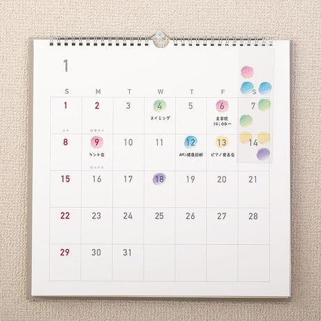Serier - Kalenderstickers Moln från Midori  - En väggkalender hänger på en vägg. På kalendern har det klistrats på små klistermärken i form av moln på vissa av datumen. Tidformera