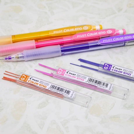 Color Eno Färgstift 0,7 - Violet från Pilot Pen. Tre stiftpennor i färgerna gul, rosa och lila ligger på ett bord. Bredvid ligger tre öppnade förpackningar med stift. Stiften i är i färgerna orange, rosa och lila.  - Tidformera