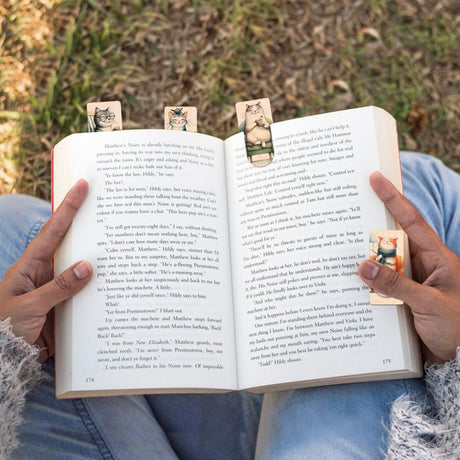 Små bokmärken av trä fastsatta i en öppen bok. På bokmärken finns glada katter. Wooden Booktags - Happy Kitties från Cozywood - Tidformera